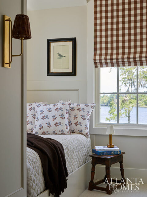 Bedroom with a bed, floral pillows, brown blanket, and a window with a gingham shade.