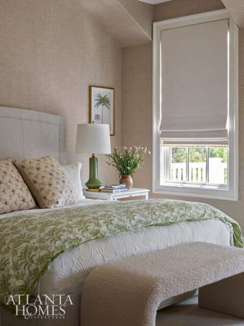 Bedroom with textured beige walls, upholstered headboard, green lamp, and botanical print bedding.