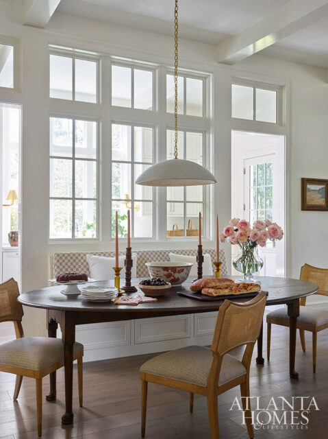 Dining room with oval table, cane-backed chairs, and large windows.