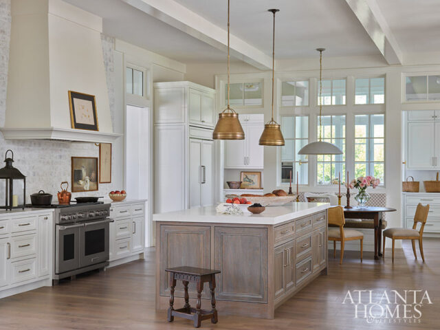White kitchen with large island, stainless steel range, and brass pendant lights.