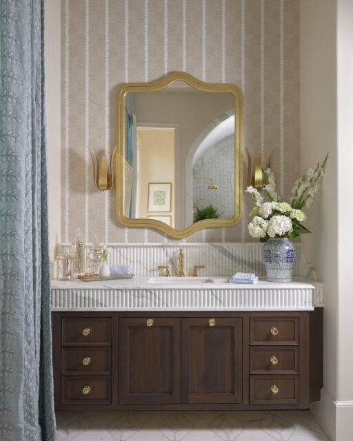 Bathroom vanity with dark wood cabinets, marble countertop, gold mirror, and patterned wallpaper.