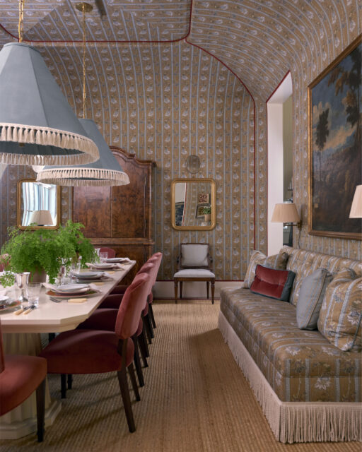 Dining room with floral wallpaper, velvet chairs, and a patterned sofa.