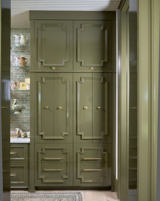 Olive green cabinets with brass hardware and geometric detailing. Shelves with decorative items