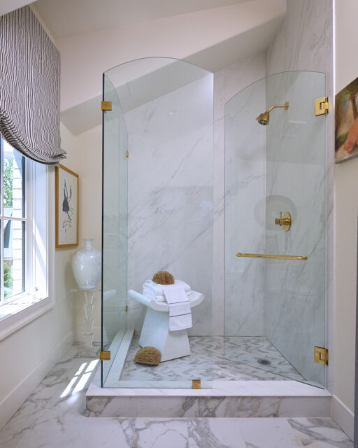 Marble shower with glass enclosure, gold fixtures, and patterned tile floor.