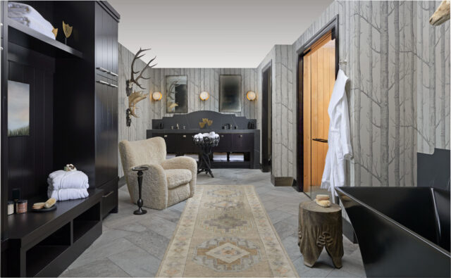 Bathroom with tree-patterned wallpaper, black vanity, sheepskin chair, and black bathtub.