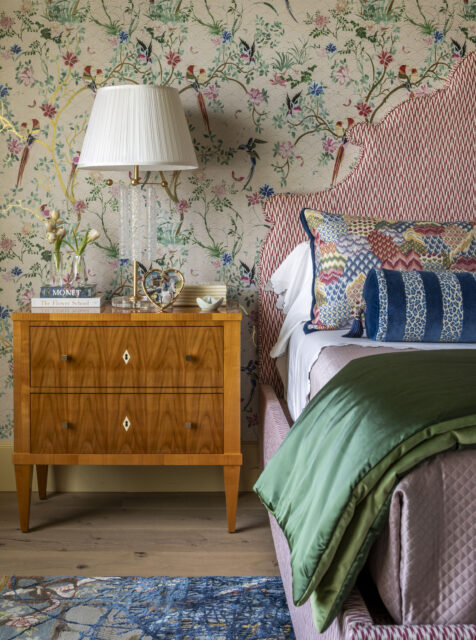 Bedroom with floral wallpaper, red patterned headboard, wooden nightstand, and green bedding.