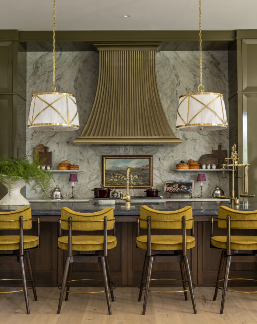Kitchen island with marble backsplash, brass range hood, and yellow bar stools.