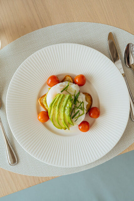 Poached egg with sliced avocado, cherry tomatoes, and toast on a white plate
