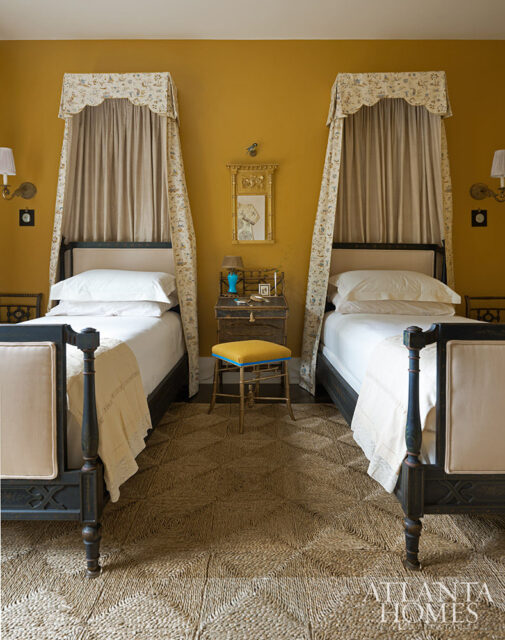 Bedroom with two twin beds, mustard yellow walls, and patterned canopy drapes.