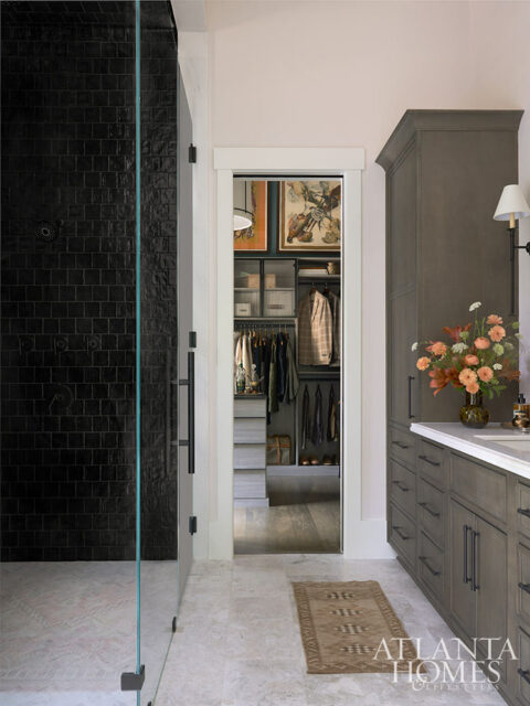 Walk-in closet with gray cabinetry and clothing, adjacent to a bathroom with a black tiled shower