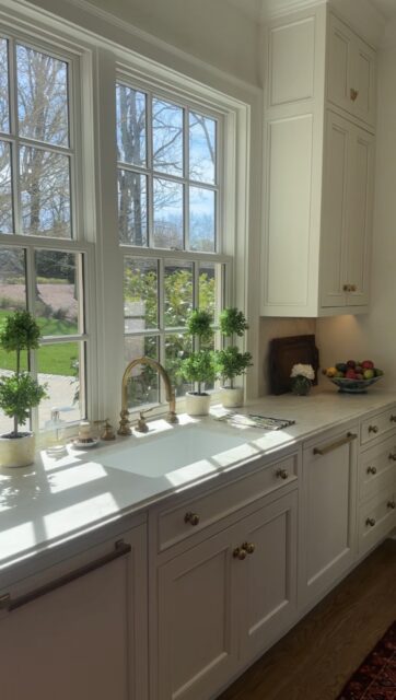 White kitchen with marble countertop, brass faucet, and paneled cabinets.