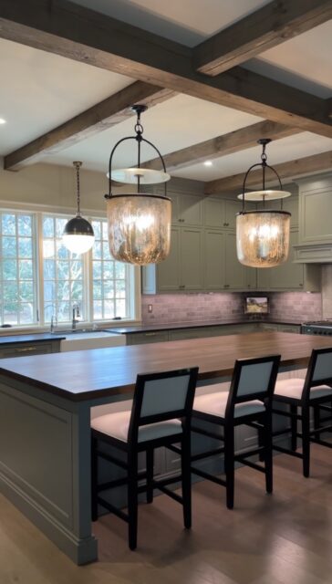 Kitchen with sage green cabinets, wood island, and pendant lights. Rustic beams on ceiling.