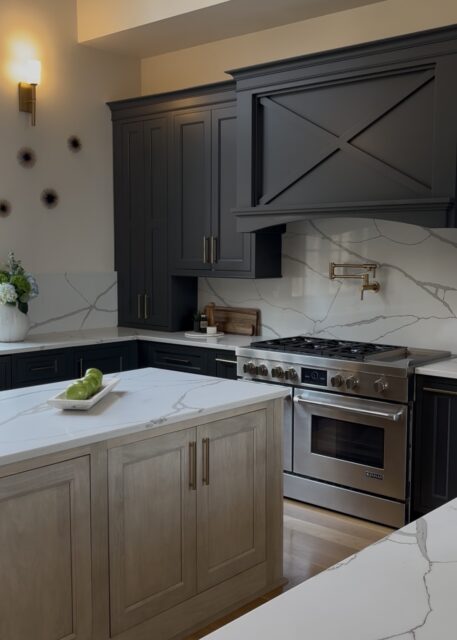 Kitchen with dark gray cabinets, marble backsplash, stainless steel range, and light wood island.