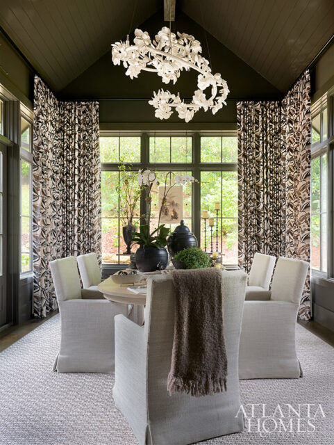 Dining room with floral curtains, light upholstered chairs, and a white floral chandelier.