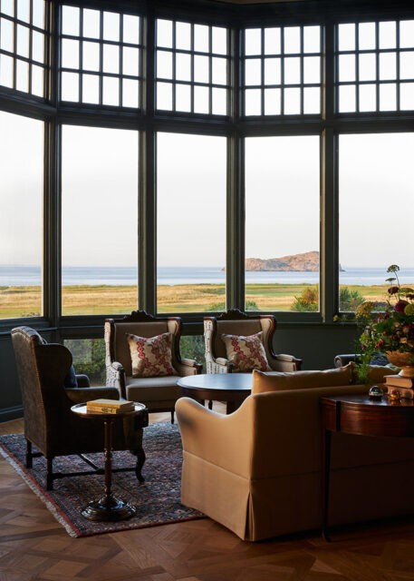 Lounge with wingback chairs, patterned pillows, and a bay window overlooking the sea