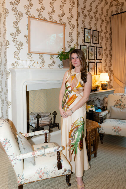 Woman in floral dress standing in a room with floral wallpaper and fireplace