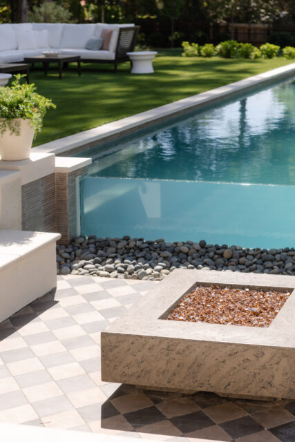 Backyard with infinity pool, glass wall, fire pit, and outdoor seating area.