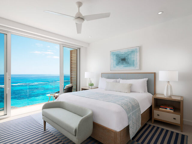 Bedroom with king bed, blue headboard, and ocean view through sliding glass doors.