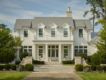 White clapboard house with gray shingle roof, dormer windows, and covered porch with columns.