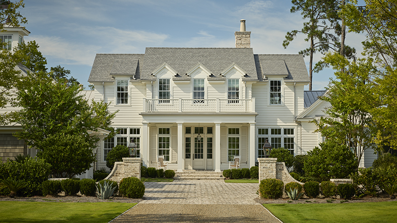 White clapboard house with gray shingle roof, dormer windows, and covered porch with columns.