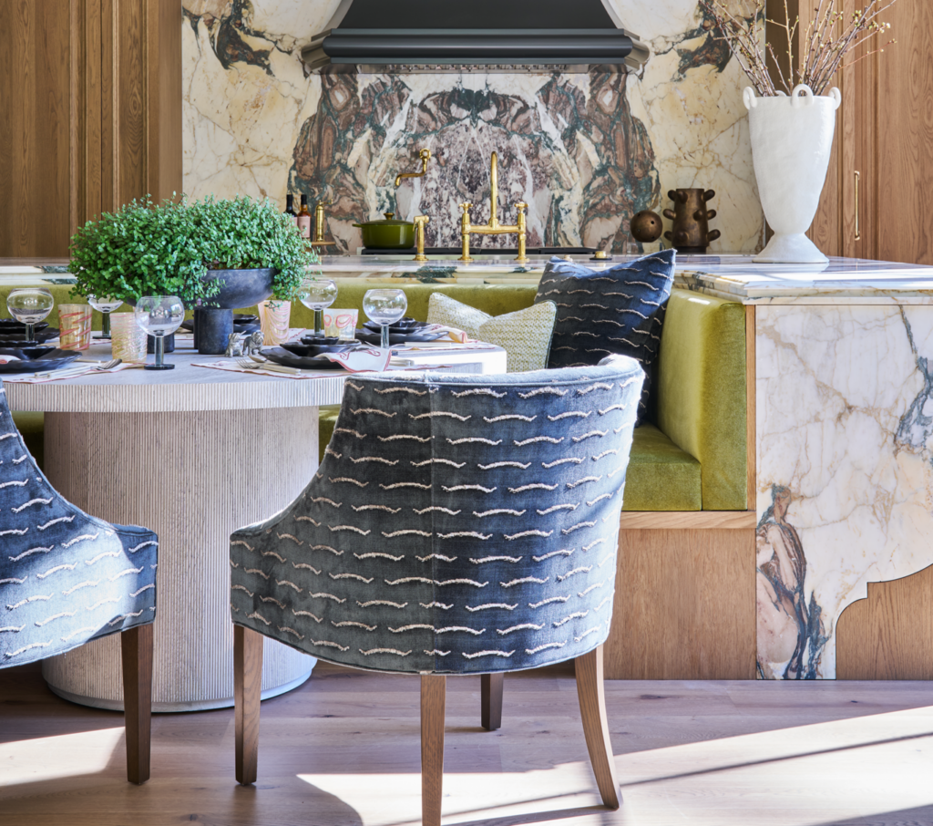 Dining area with blue patterned chairs, green banquette, marble backsplash, and round table