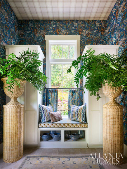 Window seat with blue floral wallpaper, patterned pillows, and large woven planters.