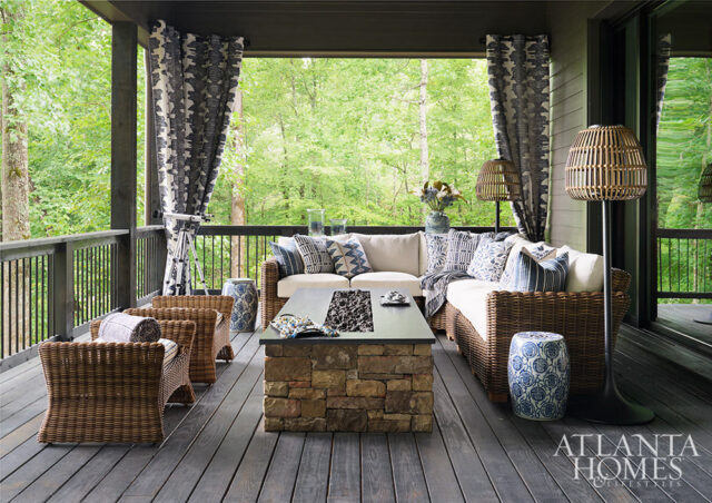 Covered porch with wicker sectional, stone fire pit table, and blue and white patterned pillows.