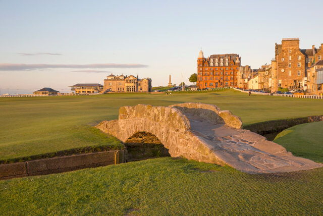 Stone bridge over a stream on a golf course with buildings in the background