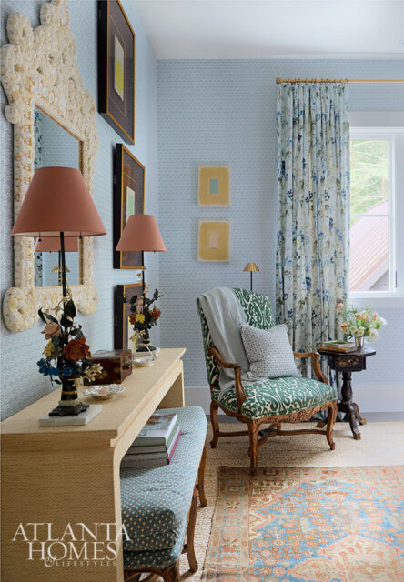 Light blue patterned wallpaper, console table with lamps, green patterned armchair, and floral