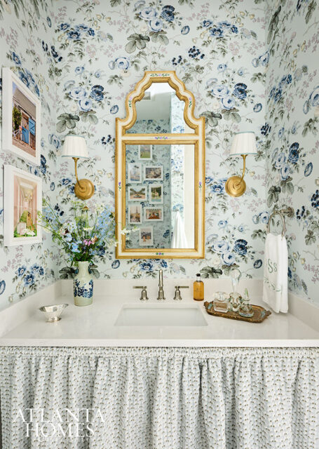 Powder room with blue floral wallpaper, gold mirror, and white vanity with skirt