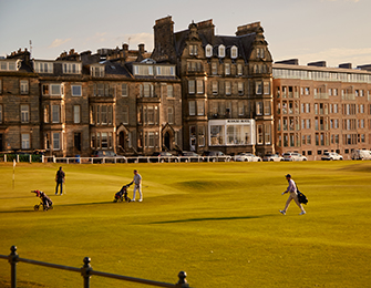 Golfers on a green course with a large stone building in the background.