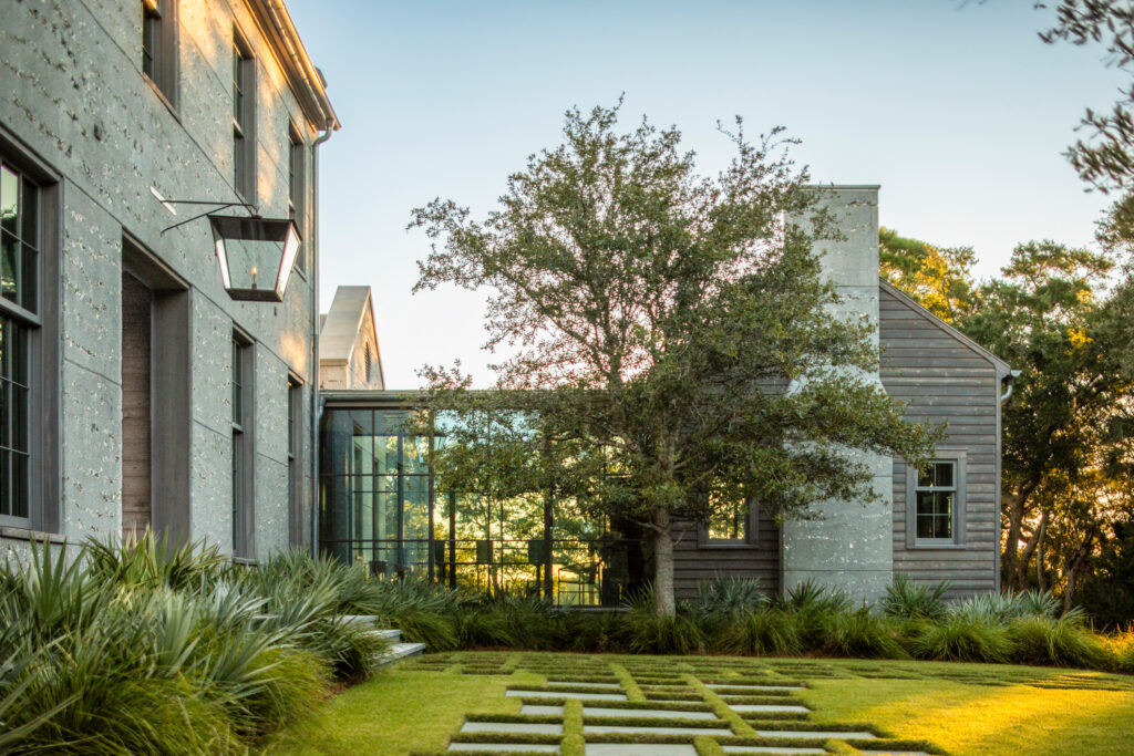 Modern home with gray stone and wood siding, glass walkway, and geometric lawn design.