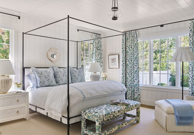 Bedroom with black canopy bed, blue floral pillows, white bedding, and floral bench.