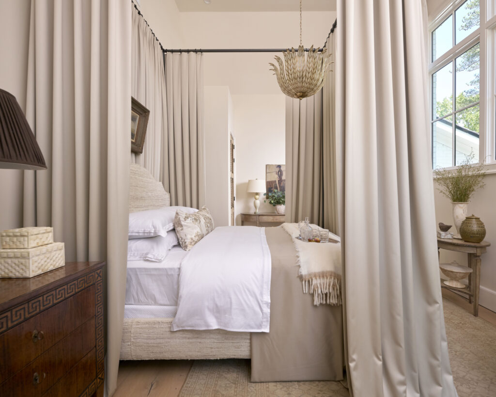 Bedroom with a four-poster bed, draped in cream curtains, and a decorative chandelier.