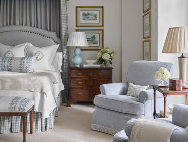 Bedroom with upholstered headboard, patterned pillows, and light blue armchairs.