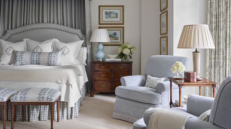 Bedroom with upholstered headboard, patterned pillows, and light blue armchairs.