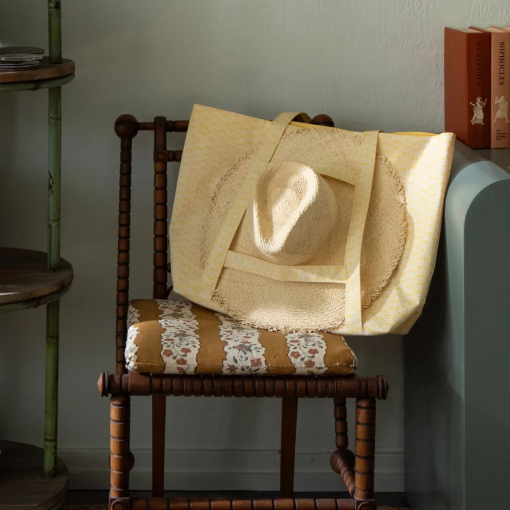 Wooden chair with striped floral cushion, straw hat, and yellow patterned tote bag