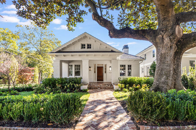 White brick house with gabled roof, brick walkway, and mature tree