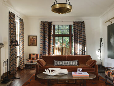Living room with rust sofa, patterned chairs, fireplace, and large abstract art