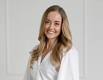 Woman with blonde hair smiling, wearing a white button-up shirt.