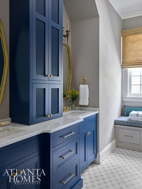 Blue bathroom vanity with marble countertop and brass hardware. Tall cabinet with fluted doors.