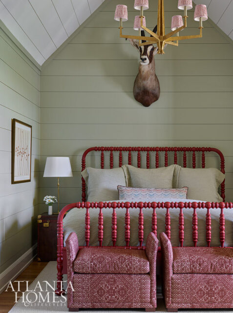 Bedroom with red spindle bed, taxidermy antelope head, and patterned benches.