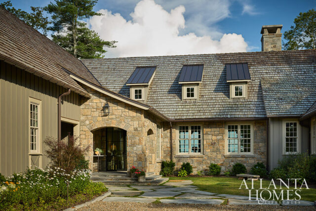 Stone and wood-sided house with arched entryway, dormer windows, and stone chimney.