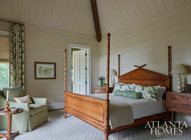 Bedroom with wood four-poster bed, green patterned pillows, and shiplap walls.