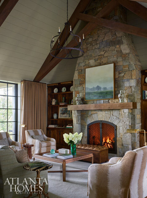 Living room with stone fireplace, wood beams, built-in bookshelves, and upholstered seating.