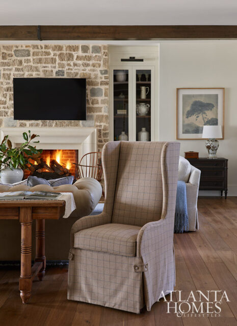 Living room with stone fireplace, wingback chair, and wooden table.