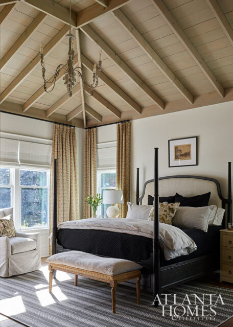 Bedroom with dark wood four-poster bed, upholstered headboard, patterned curtains, and vaulted wood
