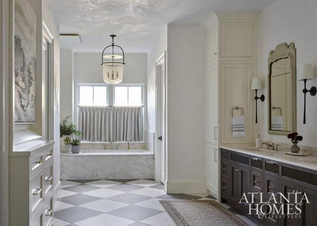 Bathroom with marble tub, diamond tile floor, dark wood vanity, and cream cabinetry.