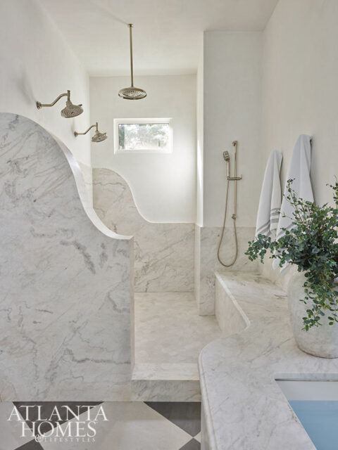 White bathroom with marble shower walls, multiple shower heads, and a small window.