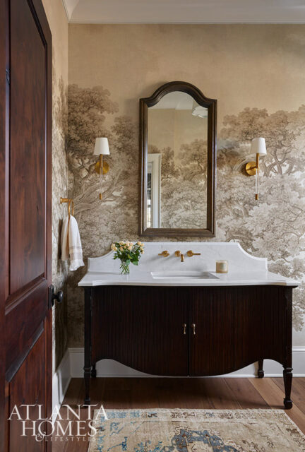 Dark wood vanity with fluted doors, marble countertop, and arched mirror above. Toile wallpaper and